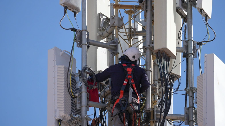 Technician checking equipment and cables on a modern mobile network antenna,